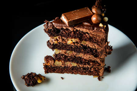 closeup piece of tasty chocolate cake with creamy inter layer decorated with chocolate candy served on white plate on black backgroundの写真素材
