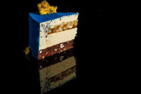 piece of blue mousse cake with yellow sponge cake decoration on top and caramel pear inter-layer stands on black mirror backgroundの写真素材