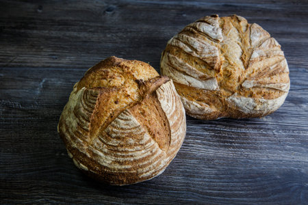 two whole tasty handmade round white wheat bread lie on  dark wooden table