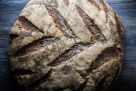 big whole homemade round black bread with interesting texture lie on dark wooden table