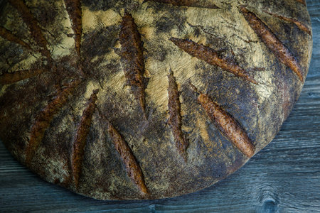 macro  big whole handmade round black bread with interesting texture lie on dark wooden table