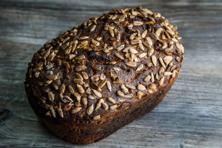 top view of whole tasty handmade rectangular black bread with sunflower seeds on top lie on dark wooden backgroundの写真素材