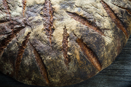 closeup big whole handmade round black bread with interesting texture lie on dark wooden table