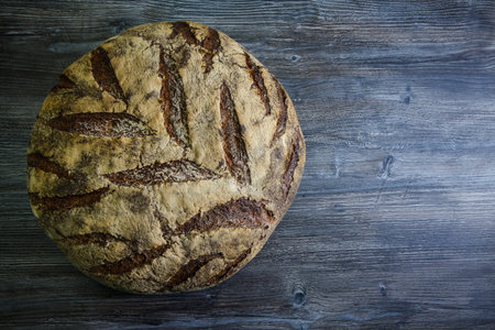 top view of big whole handmade round black bread with interesting texture lie on dark wooden table