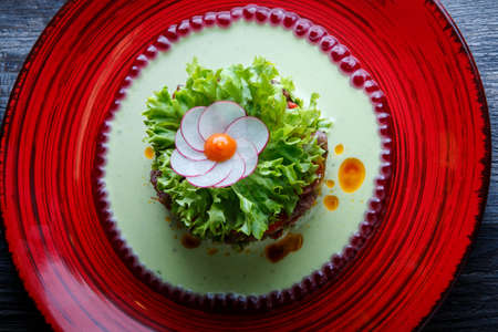 top view on healthy green salad with meat and flower decoration made from radish on red restaurant plate on wooden tableの写真素材