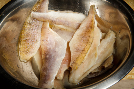 closeup group of raw hake fillet parts stacked in metal bowl
