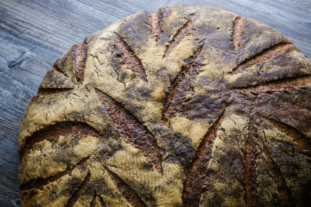 macro  big whole handmade round black bread with interesting texture lie on dark wooden table