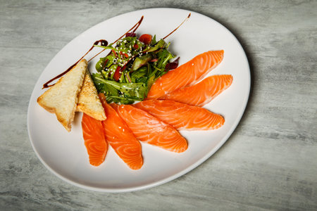 Salmon slices served with rucola and tomato salad and toasted bread on white restaurant plate