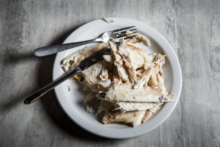 torn cooked fish fillet served with fork and knife on white restaurant plate stand on gray table...