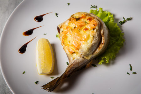 closeup baked trout served with cheese and salmon stuffing, salad leaf, lemon and sauce on white...