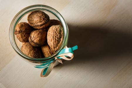 top view on standard open glass jar filled with whole walnuts decorated with blue and white ribbons stand on kitchen tableの写真素材