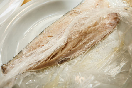 one divided part of raw mackerel fillet with bones lie in food film on white plate