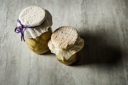top view two small glass jars with homemade canned sliced zucchini decorated with handmade lid stand...