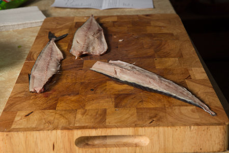 three divided part of raw mackerel fillet with bones lie on wooden tray on kitchen table