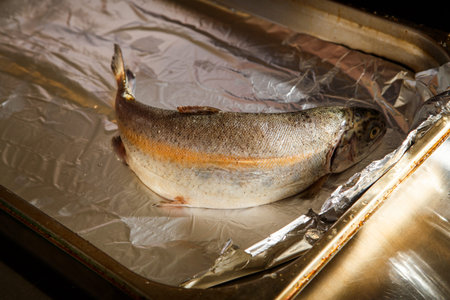closeup raw whole trout lies on parchment for baking foil on metal trayの写真素材