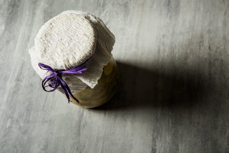 top view of small jar covered with handmade tissue and purple ribbon stand on grey table