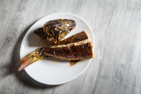 white restaurant plate served with head and tail of roasted stuffed fish on grey tableの写真素材