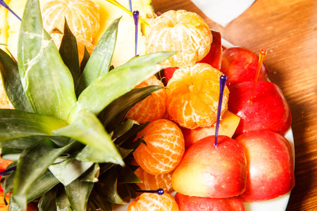closeup sliced apples, pineapples and tangerines served on white plateの写真素材