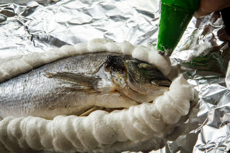 covering dorado stuffed with herbs on foil with whipped egg whites with saltの写真素材