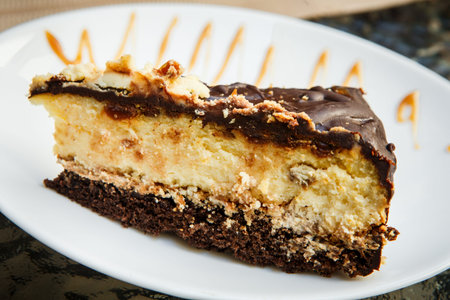 closeup  small piece of cheesecake with chocolate with caramel watering lies on white plate