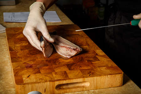 cook hand in glove prepare raw mackerel fillet with knife on wooden chopping boardの写真素材