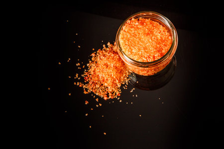 top view of small glass jar with big orange natural organic sea salt and little pile of salt stands...