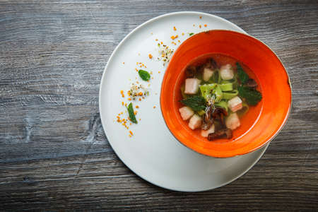 top view delicious noodle soup with mushrooms, meat, and nettle leaves served in deep restaurant bowl on wooden tableの写真素材