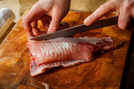 closeup chef, hands cut cleaned fish fillet by knife on brown wooden cutting board