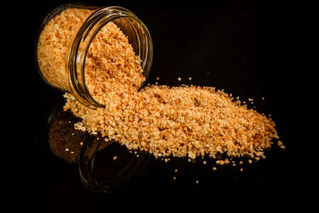 big yellow natural organic sea salt poured out from small glass jar on black mirror backgroundの写真素材