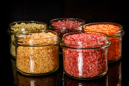 closeup small glass jars filled with pink, yellow, orange, green and red colorful sea salt on black mirror backgroundの写真素材