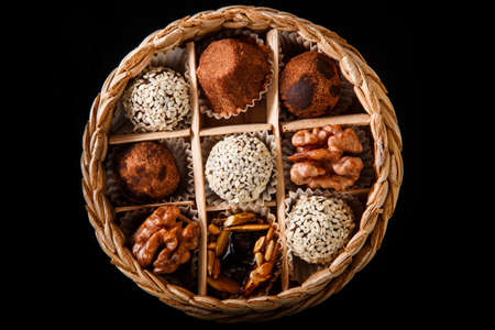 top view on small handmade box filled with assorted healthy useful handmade candies decorated with caramelized sunflower and pumpkin seeds, cocoa powder, walnut and sesame seeds on black mirror backgroundの写真素材