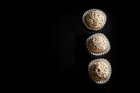 top view three healthy useful round organic handmade candies decorated with white sesame seeds on black mirror backgroundの写真素材
