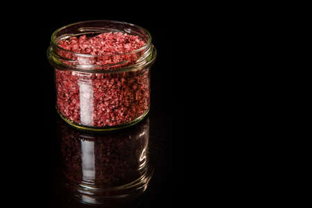 small glass jar with big red natural organic sea salt stands on black mirror backgroundの写真素材