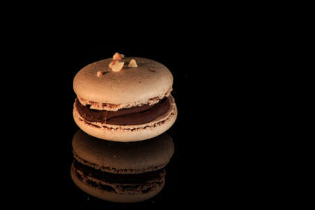 closeup beige peanut macaroon with chocolate filling served on black mirror background with reflectionの写真素材