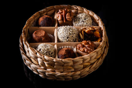 small handmade box filled with assorted healthy useful handmade candies decorated with caramelized sunflower and pumpkin seeds, cocoa powder, walnut and sesame seeds on black mirror backgroundの写真素材