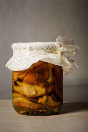 homemade canned mushrooms in glass jar stand on kitchen table against gray wall backgroundの写真素材
