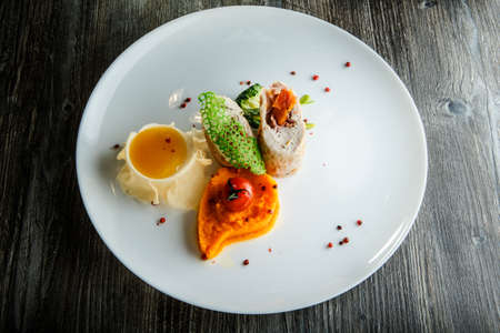 delicious dissected stuffed chicken with pumpkin puree, grilled tomato and yellow sauce on restaurant white plate on wooden tableの写真素材