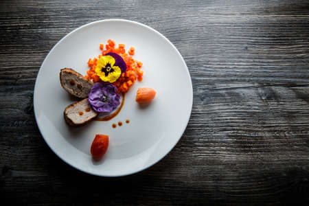 top view two pieces of grilled meat served with sweet pepper and pumpkin salad decorated with flowers on white restaurant plate on wooden tableの写真素材
