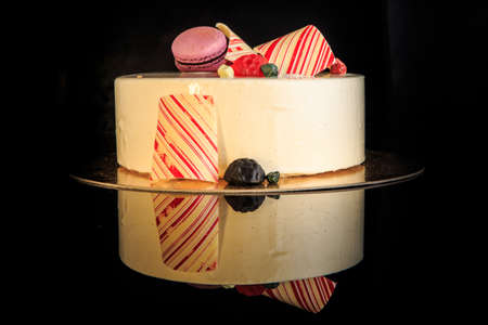 delicious round cake with white glaze decorated with purple macaron, colored chocolate and marmalade served on black backgroundの写真素材