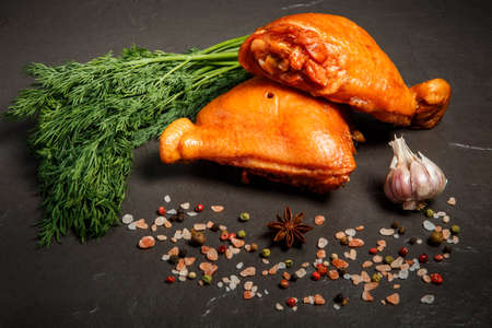 two smoked chicken thighs decorated with fresh green dill, garlic and spices served on black backgroundの写真素材