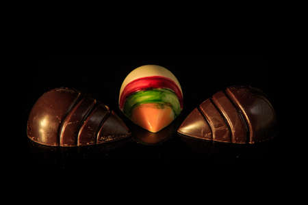 set of three shell-shaped black and white chocolate candies with colorful decoration served on black backgroundの写真素材