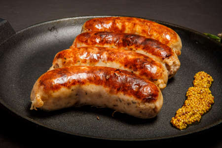 macro view four fried sausages on round black pan decorated with granular mustard served on black backgroundの写真素材