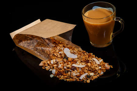 big cup of coffe and scattered from open craft bag granola with dried coconut and raisins on black backgroundの写真素材