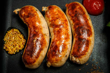 top view closeup square pan with three fried sausages, ketchup and caraway seeds served on black backgroundの写真素材