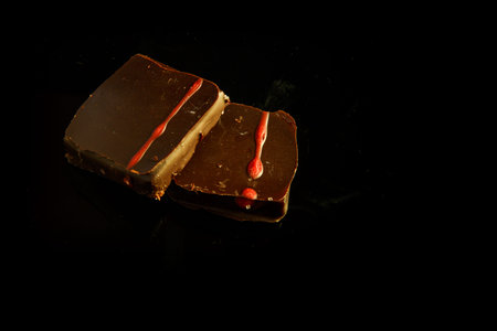 top view of two small square chocolate candies decorated with red caramel served on black background