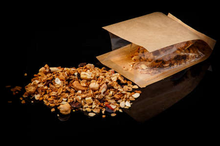 granola with cashew, peanuts, walnuts, and dried cacao scattered from kraft paper bag on black backgroundの写真素材