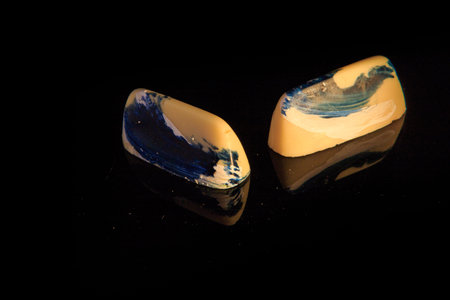 closeup two long white chocolate candies with blue art decoration served on black mirror background