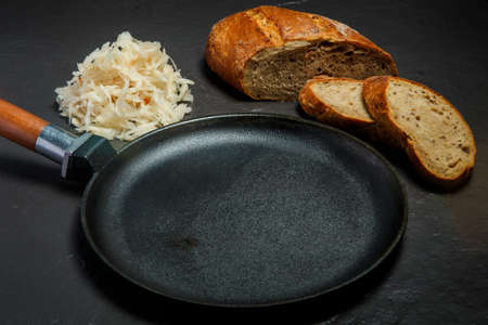 Top view on empty large black frying pan served with sliced rye bread and homemade sauerkraut on black backgroundの写真素材