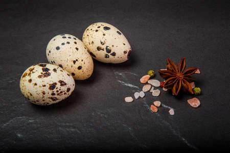 Closeup three small quail eggs served with pink Himalayan salt and different spices on black backgroundの写真素材