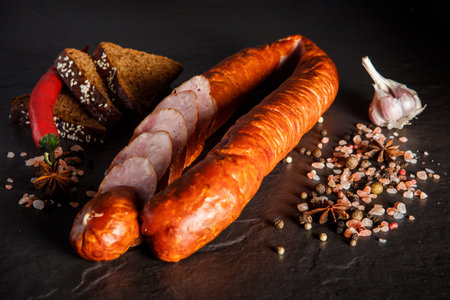 Sliced circle of smoked ham sausage with sliced pieces served with spices, garlic, rye bread, and...